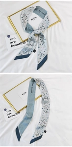 Detail view of a Morandi blue floral silk scarf tied elegantly on a soft white fabric