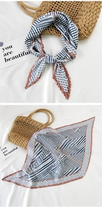 Detail of blue and white striped square silk scarf with pleated edges on a white fabric