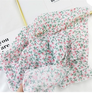 Detailed close-up of white floral cotton linen scarf with small pink flowers and green leaves