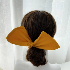 Detail of bright yellow fabric bow hair clip on dark brown braided bun hair