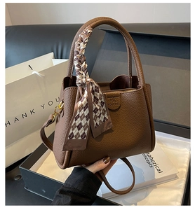 Close-up of brown litchi leather bucket bag featuring a decorative silk scarf handle