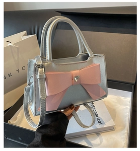 Detail of silver textured leather bag featuring a pink bow and heart rhinestone accent