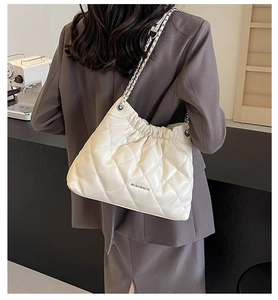 Close-up of beige quilted bucket bag with chain strap worn by a model in a suit