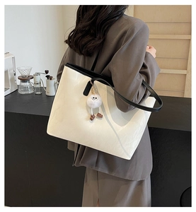 Detailed back view of a large white tote bag with black handles and a cute plush doll charm