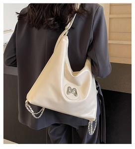 Detail of cream hobo bag featuring silver M logo and decorative metal chain strap