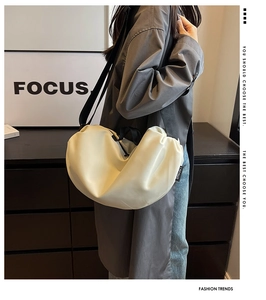 Detail view of the side label on a cream dumpling crossbody bag with black textile strap