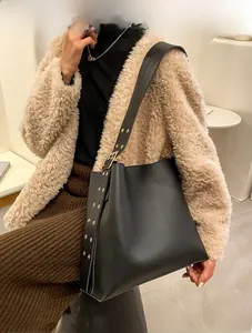 Détail d'un sac seau en cuir noir avec large bandoulière à œillets métalliques dorés
