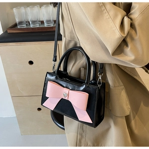 Detailed view of black crossbody bag featuring a large pink bow and heart rhinestone