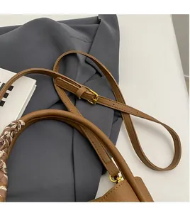 Detail of brown leather handbag with adjustable strap and scarf-wrapped handle