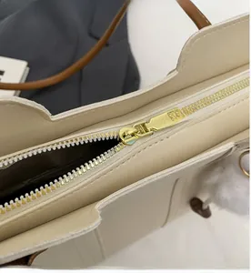 Close-up of smooth gold metal zipper on cream white leather tote bag for women