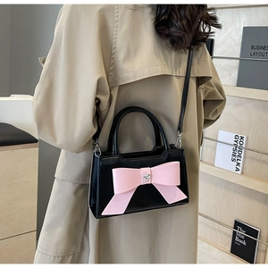 Detail of a black patent leather handbag with a pink bow and heart crystal on a model
