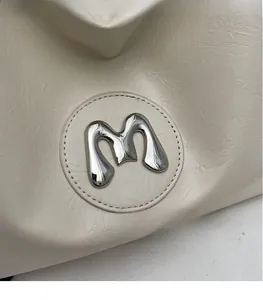 Detail of the vintage beige pleated leather bag with a 3D silver metal M logo emblem