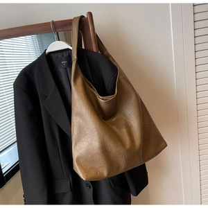 Détail d'un grand sac cabas marron vintage avec texture en cuir souple sur un cintre en bois
