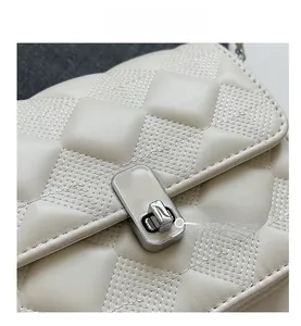 Detail of silver metallic twist lock on beige quilted crossbody bag leather surface