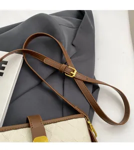 Détail de la bandoulière en cuir marron réglable et dorures sur le sac seau blanc cassé
