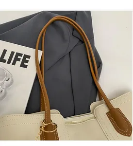 Close-up of the reinforced brown leather handle and gold chain on the cream tote bag