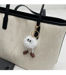 Detail of white plush cartoon charm with big eyes and shoes on a white tote bag