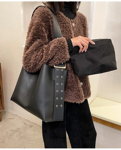 Détail du sac seau noir en cuir avec large bandoulière à œillets et pochette assortie