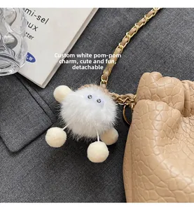 Detail view of a cute white plush charm on a gold metal chain for a leather bag