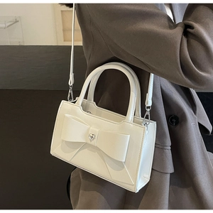 Detail of white square bag featuring large bow and heart rhinestone on leather surface