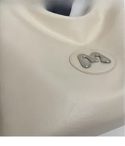 Detailed macro view of cream-white wrinkled leather texture with a metallic M logo badge