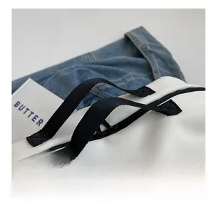 Detail showing the reinforced X-shape stitching on the white canvas bag's black handle