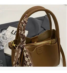 Detailed close-up of brown pebbled leather bucket bag with decorative handle scarf