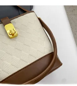 Détail du tissu texturé crème avec bordure en cuir marron et fermoir en métal doré du sac