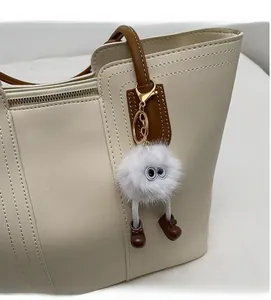 Close-up of a white fluffy plush charm with large eyes attached to a brown leather tote bag