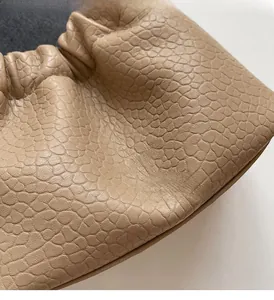 Close-up of beige leather pleated handbag detail with gold branding and lychee texture