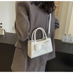 Detail of cream white leather crossbody bag with bow and heart crystal on a model
