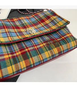Close-up of colorful plaid tote bag with gold logo and red leather piping detail