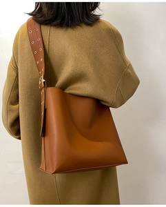 Détail d'un sac seau en cuir caramel avec une large bandoulière et des anneaux en métal