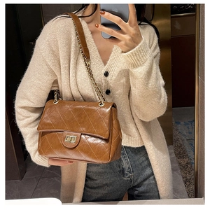 Close-up of quilted leather bag with golden square metal lock and chain strap detail