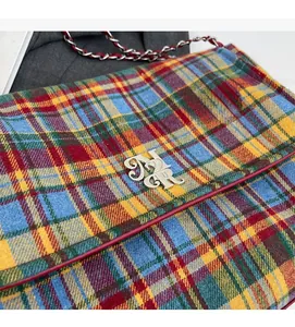 Detailed macro view of the colorful plaid fabric, silver logo, and chain strap of this tote bag