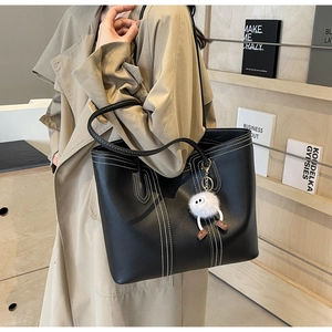 Side view of black tote bag with white stitching and plush charm on a female model