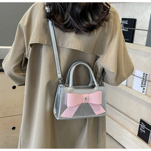 Detail of silver crossbody bag featuring a pink bow and heart-shaped crystal on the front