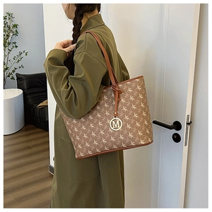Sac cabas marron à motif Pégase avec pendentif M doré porté à l'épaule sur le côté