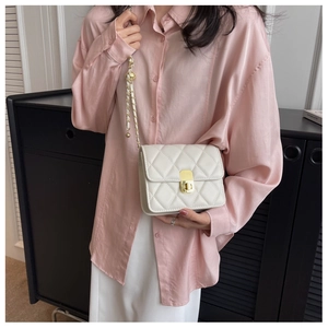 Detail of a beige quilted crossbody bag with gold chain strap worn by a model