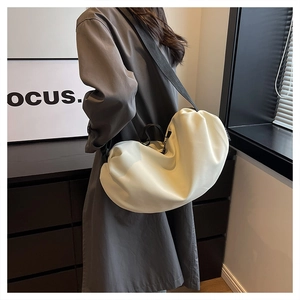 Close-up of a cream-colored crossbody cloud bag with adjustable black shoulder strap