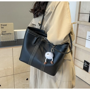 Detail of black tote bag featuring white contrast stitching and a plush charm on strap
