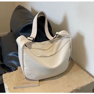 Detailed macro of a cream canvas hobo bag with adjustable strap on a stone texture surface