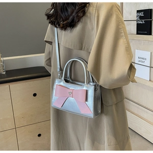 Silver square crossbody bag with pink bow accent shown being worn by a model in a room