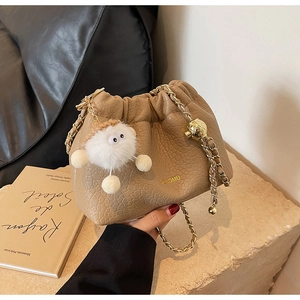 Detail of khaki pleated cloud bag with gold chain strap and plush ball accessory