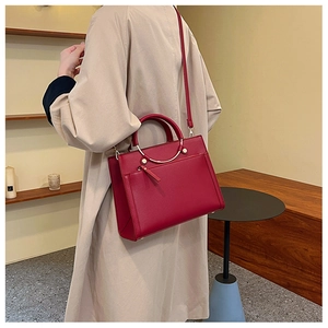 Red textured leather bridal handbag with golden metal handles shown on trench coat