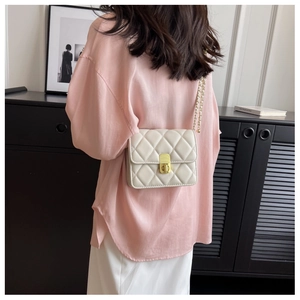 Detail of a beige quilted crossbody bag with gold chain strap on a model outfit