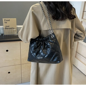 Close-up of black quilted leather bucket bag with silver chain strap on khaki coat