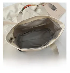 Vue détaillée du sac cabas en toile beige avec poche zippée et bandoulière brodée fleurie