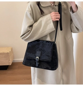Detail of black tote bag with matte texture and gold buckle on model in beige coat