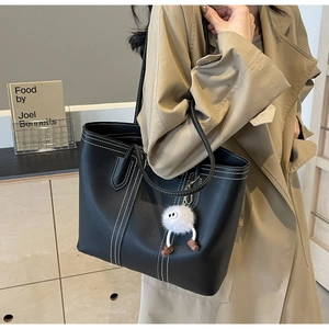 Detail of black tote bag with white stitching and plush doll charm on shoulder strap